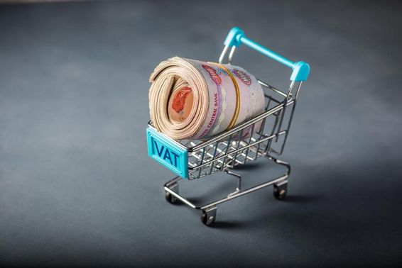 Kis bevásárlókocsi, benne köteg dirham, az elején a vat azaz adó szó.