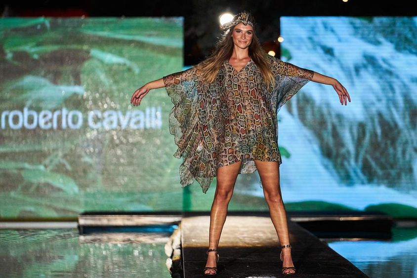 Cartel de Roberto Cavalli exhibido en el fondo, delante figura femenina en vestido de Roberto Cavalli en la pasarela.