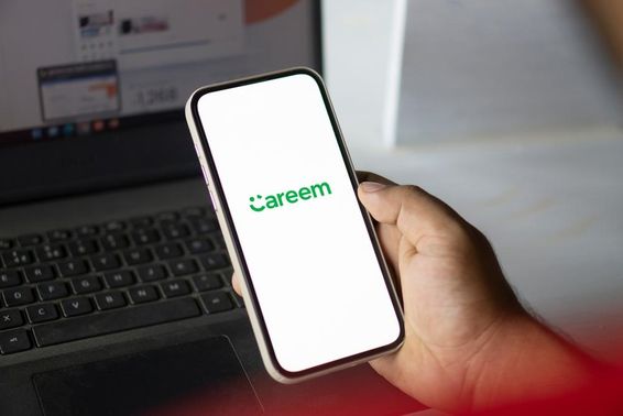手握着运行Careem应用的手机，背景中可见一本笔记本。