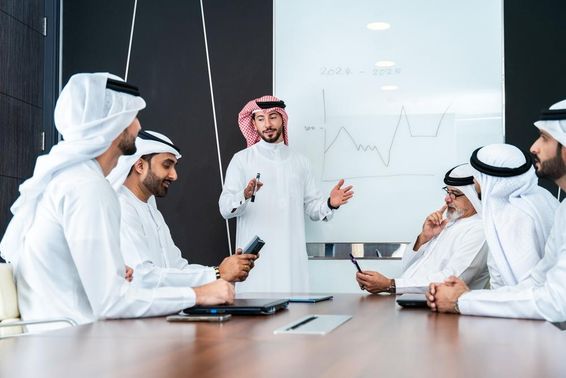 Arab tervezők beszélgetnek egy tábla előtt,  asztalon egy notebook és telefon. 