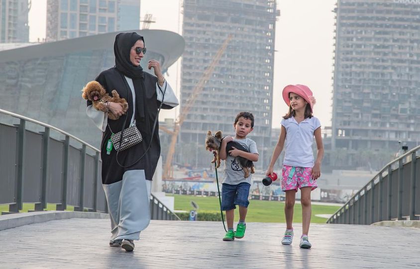 Dubai felhőkarcolok előtt egy család 2 gyerekkel, anya és ez egyik gyerek egy kutyát fog a kezében. 