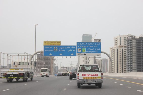Placa de sinalização rodoviária de Al Khail, com alguns prédios altos ao fundo.