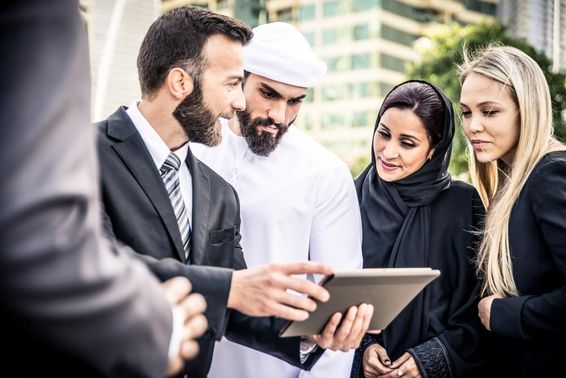 Egy európai és egy emriati férfi néz egy tabletet mellettük 2 nő egy szőke és egy emirati is figyeli.