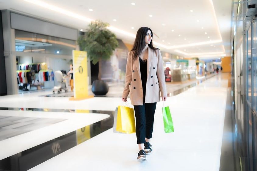 Egy nő vásárol Dubai Mal ban , kezében 2 szatyorral, háttérben a boltok almosodva. 