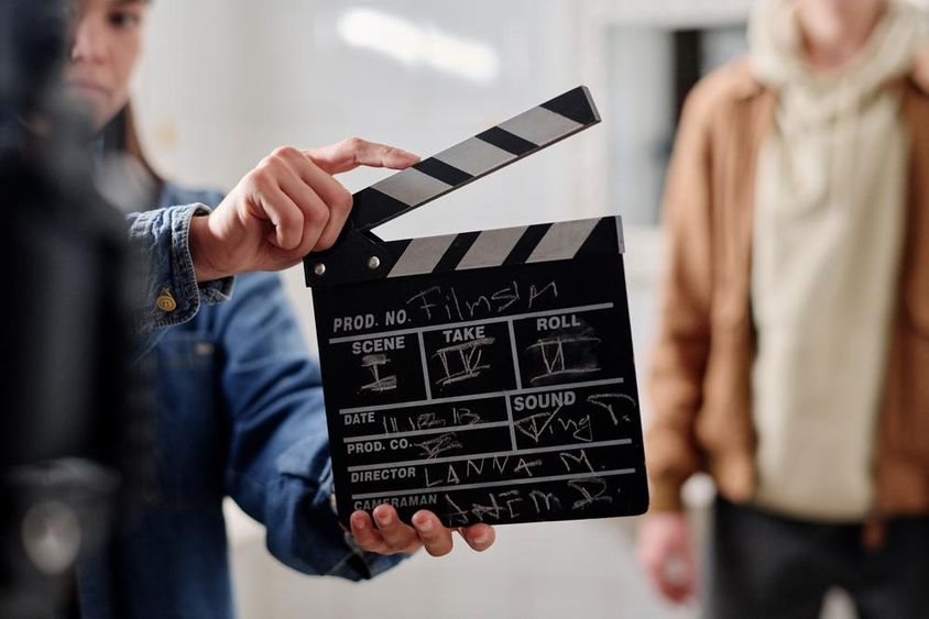 Film slate with chalk writing, two people beside it.