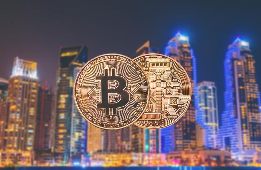 Bitcoin érmék vannak előtérbe, hátul felhőkarcolok látszanak. 
