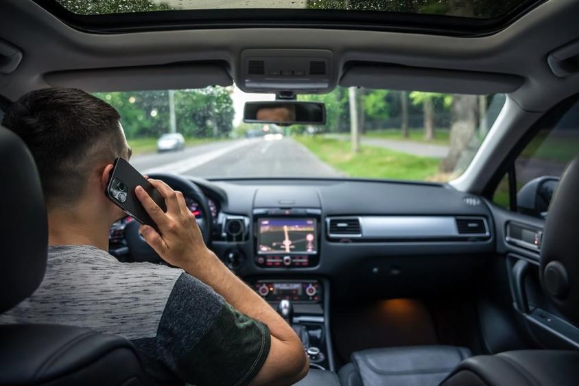 Fiatalember telefonozik vezetés közben egy autóban.