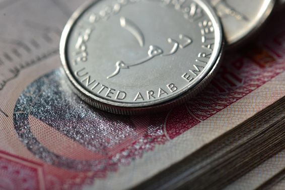 Fém egy dirham, alatta bankjegyköteg. 