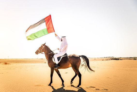 Közel-keleti férfi tipikus emírségi ruhában arab lovon lovagol a dubaji sivatagban.
