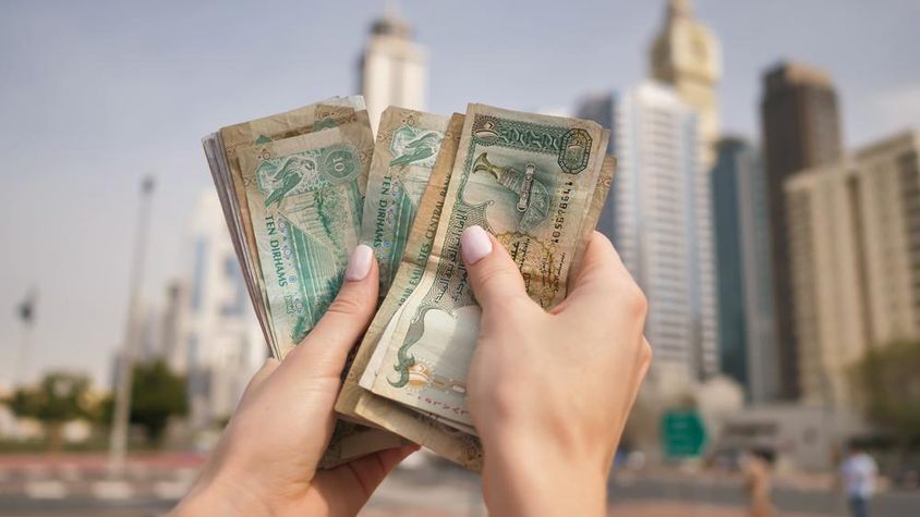Egy lány kezében az Egyesült Arab Emírségek pénze a dubaji felhőkarcolók hátterében.