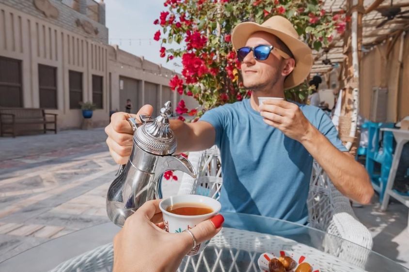 Egy férfi Dubajban egy arab kávézóban piheni ki az utazását, és egy csésze aromás kávét tölt egy dallah kávéskannából.