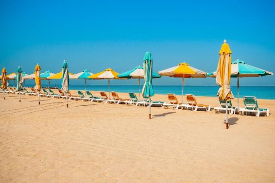 Praia pública de Dubai, areia, espreguiçadeiras e mar azul.