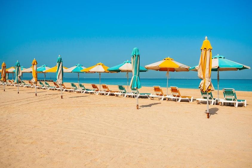 Dubai nyilvános strand, homokos part, napágyak és a kék tenger. 