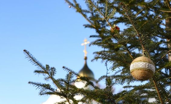 Galho de árvore de Natal com enfeites e uma cruz ortodoxa ao fundo