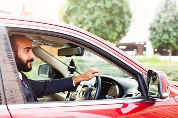 Jovem empresário dirigindo um carro alugado vermelho.