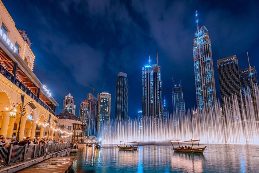 Az emberek csónakáznak, miközben a Dubai szökőkút éjszakai előadását nézik, a háttérben Dubai felhőkarcolóival.