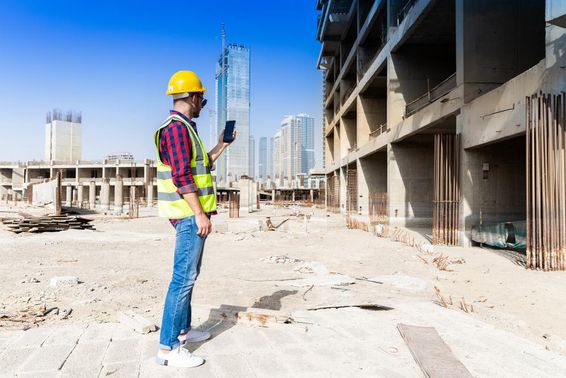 Férfi dubai építkezésen a munkája elvégzéséhez, okostelefont használ, háttérben dubai látképe.