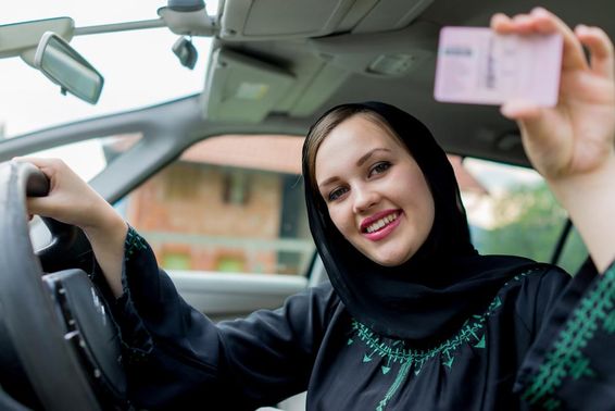 Mulher muçulmana dirigindo um carro, segurando uma carteira de motorista.