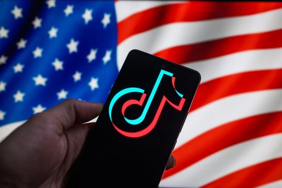A TikTok logó egy okostelefonon jelenik meg, a háttérben az Egyesült Államok zászlajával.