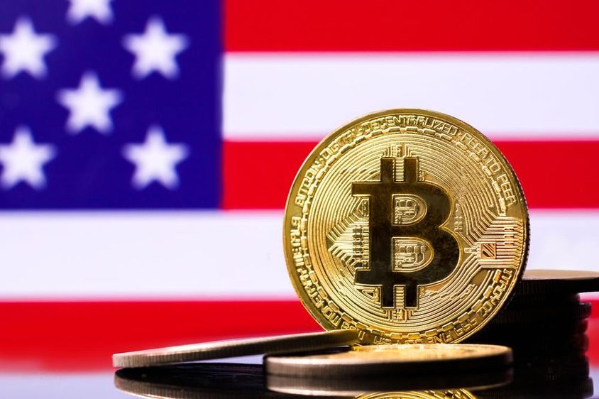 Золотая биткойн монета с флагом США на заднем плане.