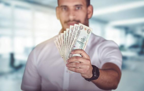 Férfi kezében egy marék Emirates dirham készpénzt.