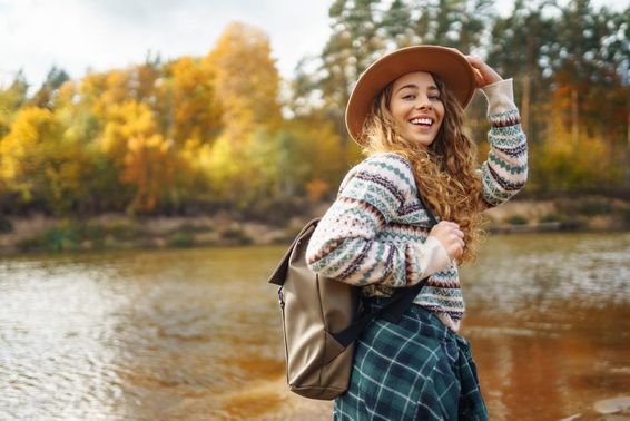 Viajante feminina com mochila e boné apreciando uma caminhada de outono ao longo de um rio.