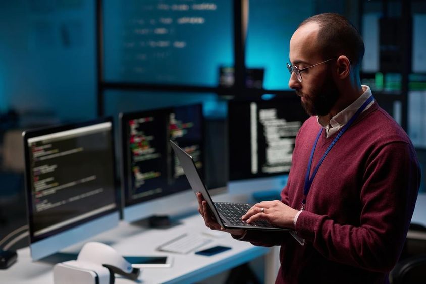 Computer programmer holding an open laptop in an IT and cybersecurity office.