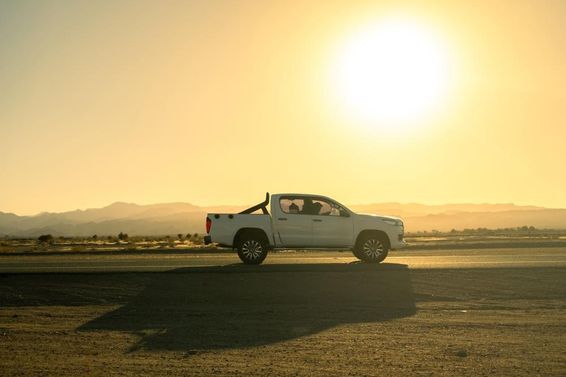 Veículo pickup branco em viagem pelo campo, dia ensolarado ao pôr do sol.