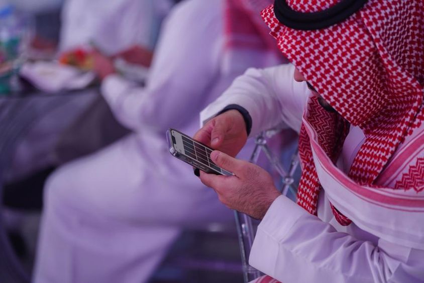 Arab férfi mobiltelefonon dolgozik, üzenetet olvas vagy gépel.