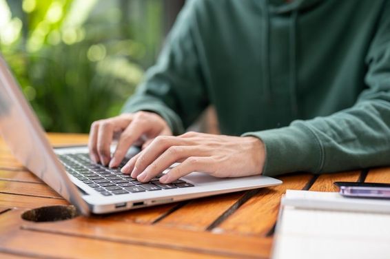 Zöld pulcsis férfi laptop távolról dolgozik egy szabadtéri asztalnál.