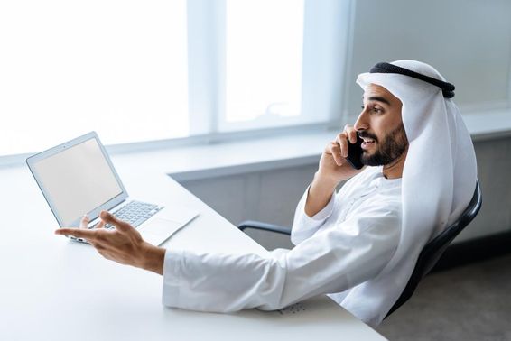 Egy sikeres üzletember hagyományos emírségekbeli fehér ruhában dolgozik dubaiban.