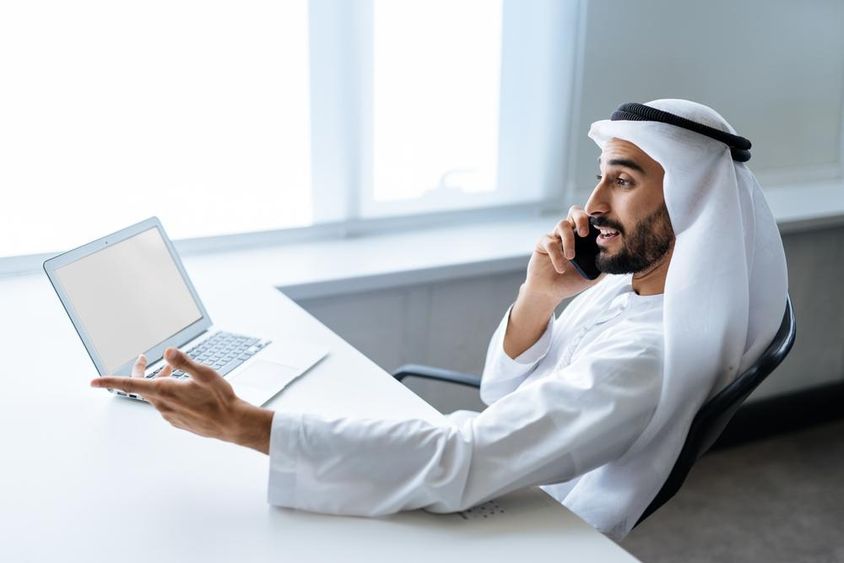 Egy sikeres üzletember hagyományos emírségekbeli fehér ruhában dolgozik dubaiban.
