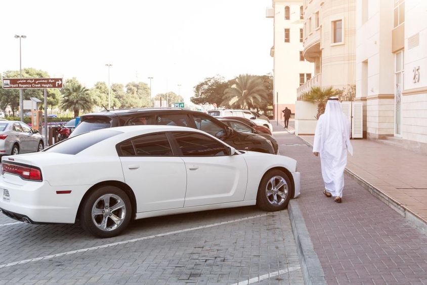 In Dubai streets: A man in national attire and a white Dodge in the parking lot.