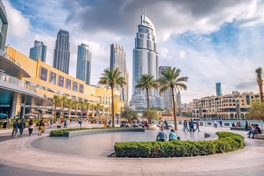 Turisták tömege sétál a Dubai Mall bejárata melletti téren és a sétányon.