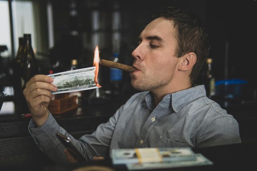 Joven apuesto encendiendo un cigarro con billete de cien dólares en un bar.
