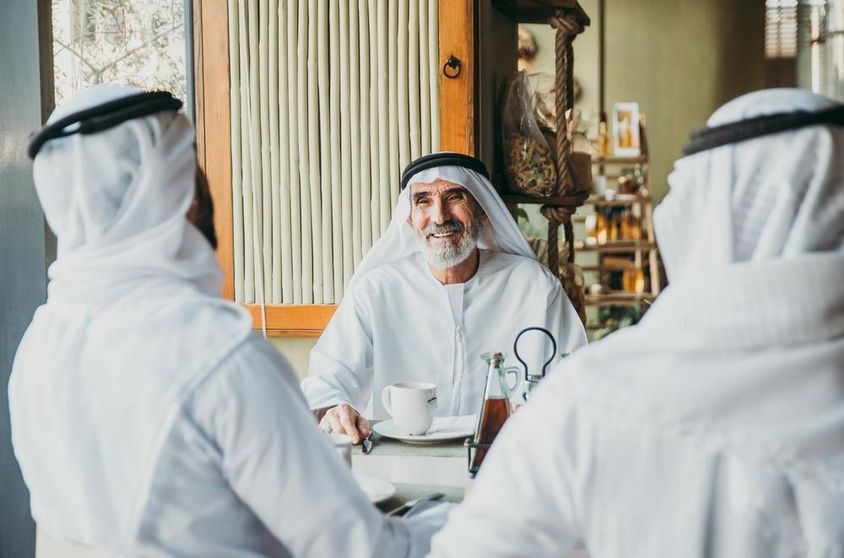 Három üzletember teázik Dubaiban hagyományos emirátusi ruhában.