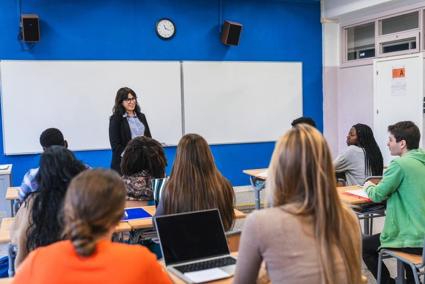 középiskolás diákok hallgatják tanárukat, amint leckét adnak egy modern osztályteremben.