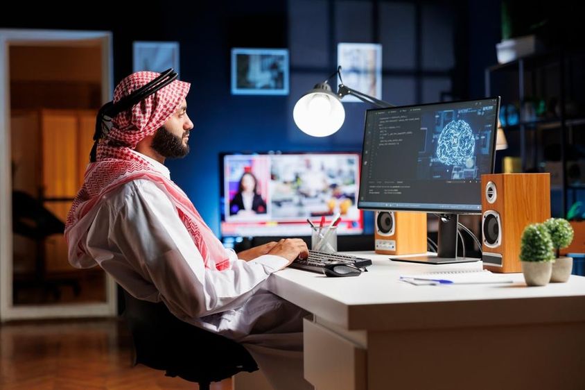 Egy arab ruhát viselő hivatásos férfi futurisztikus felhasználói felületen dolgozik.