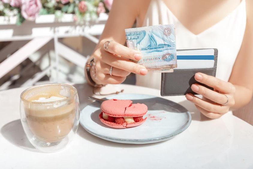 A lány fizet a reggeliért a kávézóban, dirham bankjegyekben Dubaiban.