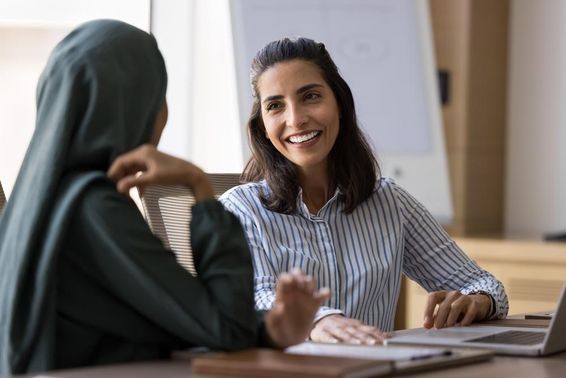 Spanisch sprechende Geschäftsfrau im Gespräch mit arabischer Kollegin.