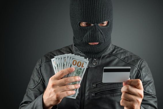 Krimineller in Skimaske hält Kreditkarte vor dunklem Hintergrund.