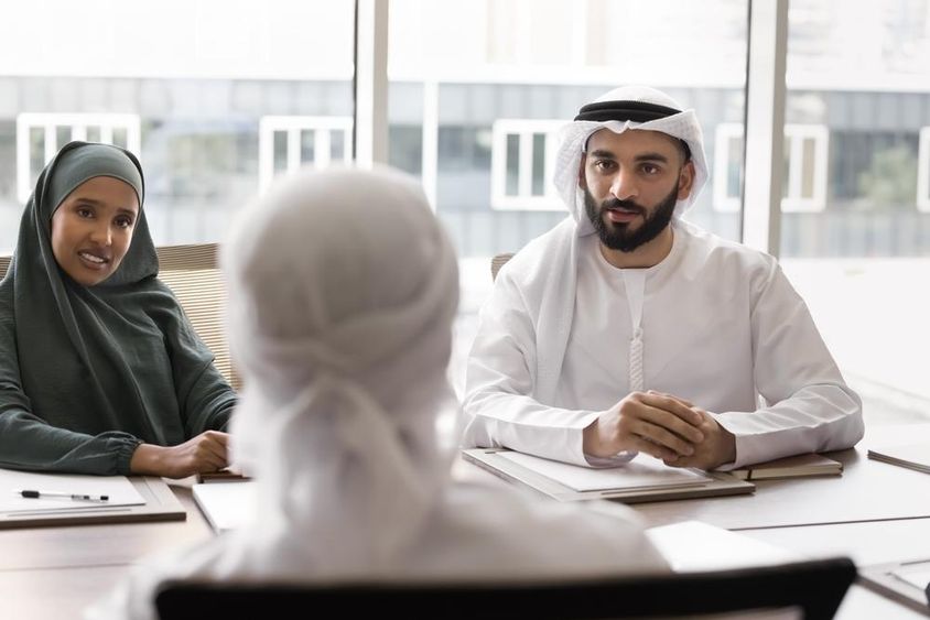 Férfi és női arab kollégák beszélgetnek az irodaasztalnál ülő partnerükkel.