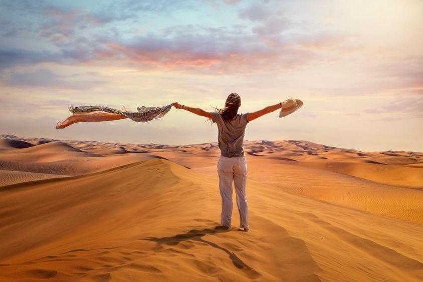 A tourist woman stands in the Red Desert, Dubai, waving her scarf in the hot air.