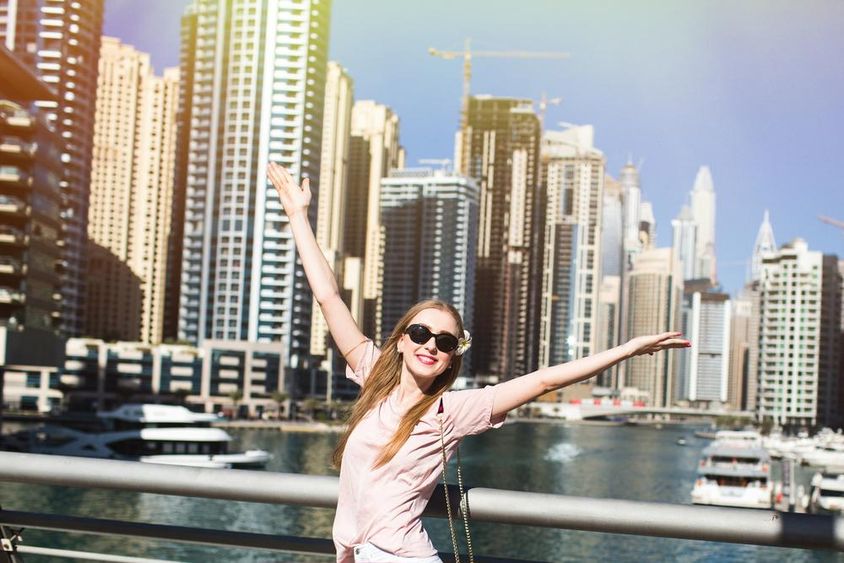 Napfény világítja meg egy csinos nőt, aki felemeli a kezét egy hídon valahol Dubaiban.