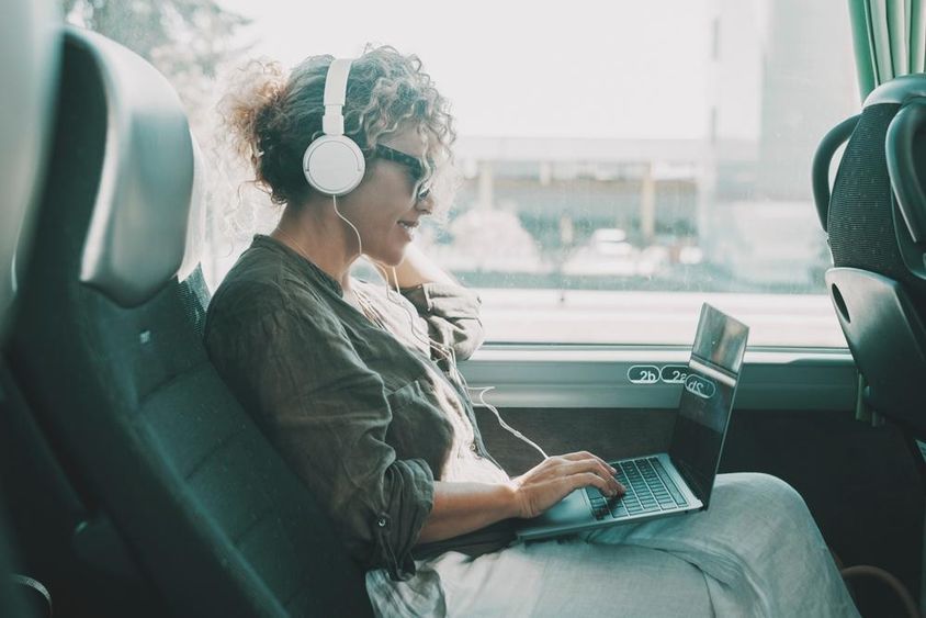 Fiatal nő laptopon dolgozik, fejhallgatóval a buszülésen ülve.