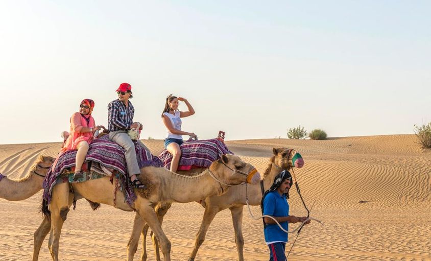 Turisták tevegelésen a Dubai sivatagban. 