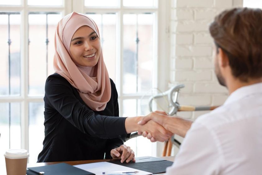 Arab női HR menedzser hidzsábban kezet ráz egy férfi állásra jelentkezővel.