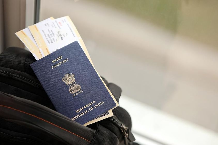 Blue Indian passport with airline tickets on a travel backpack.