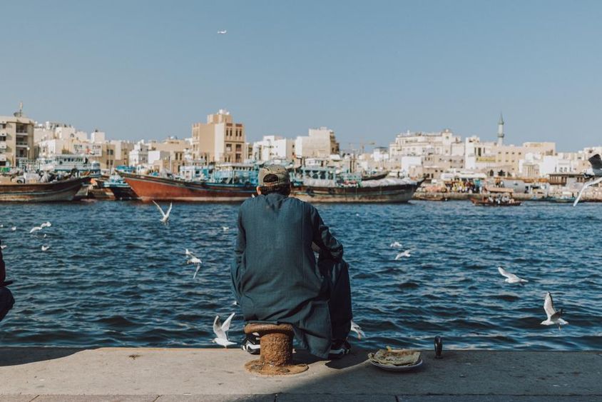 Man enjoying the waterfront view with boats and seagulls at Dubai Creek.