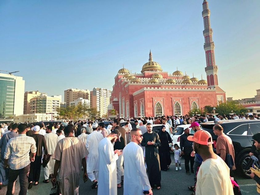 A large crowd gathered in front of a grand mosque with domes and tall minarets.